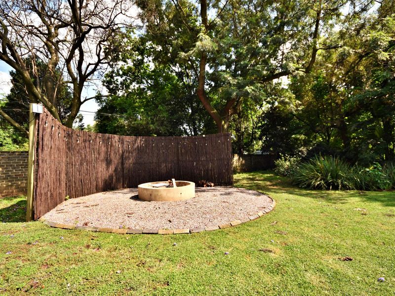 A private garden area featuring a circular gravel boma fire pit, enclosed by a decorative reed screen and surrounded by mature trees.