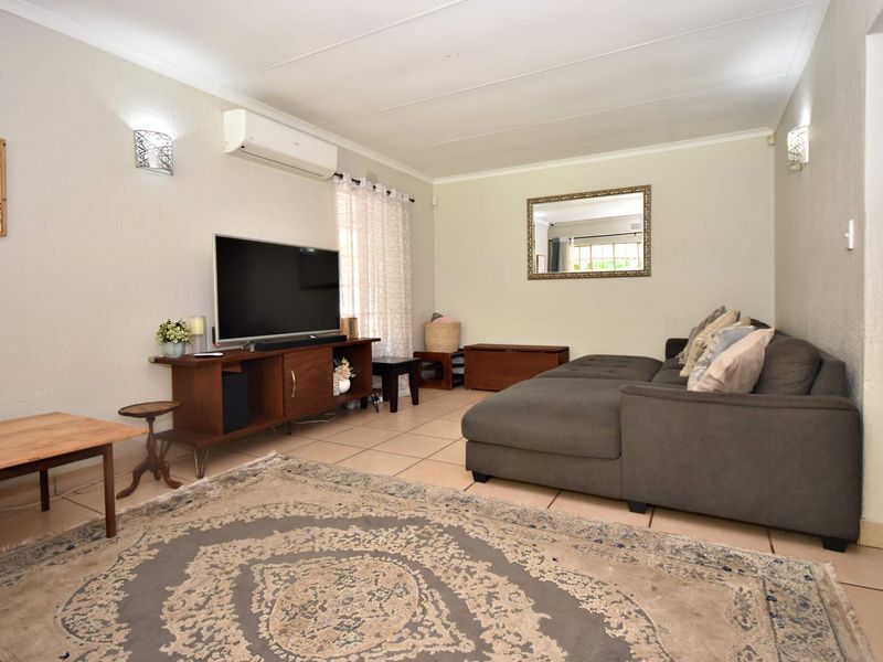 A comfortable living room featuring tiled flooring, wall-mounted lighting, and a split-system air conditioning unit.