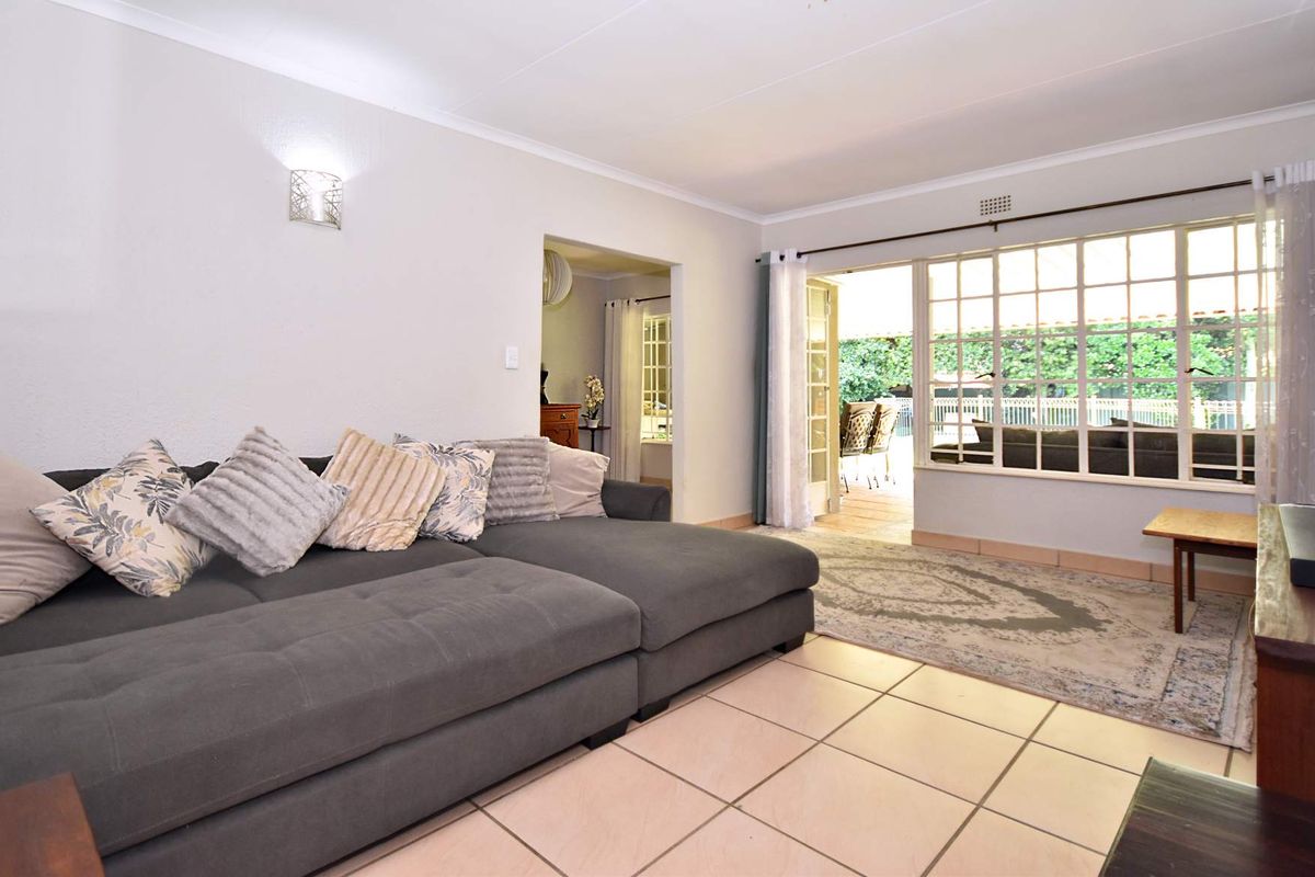 A bright living room featuring tiled flooring, a large window with grid detailing, and a sliding glass door providing access to the outdoor patio area.