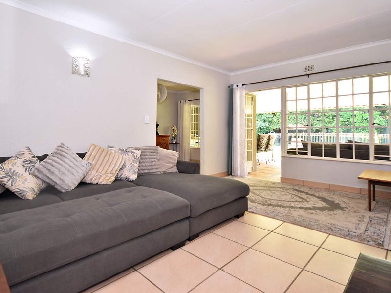 A bright living room featuring tiled flooring, a large window with grid detailing, and a sliding glass door providing access to the outdoor patio area.