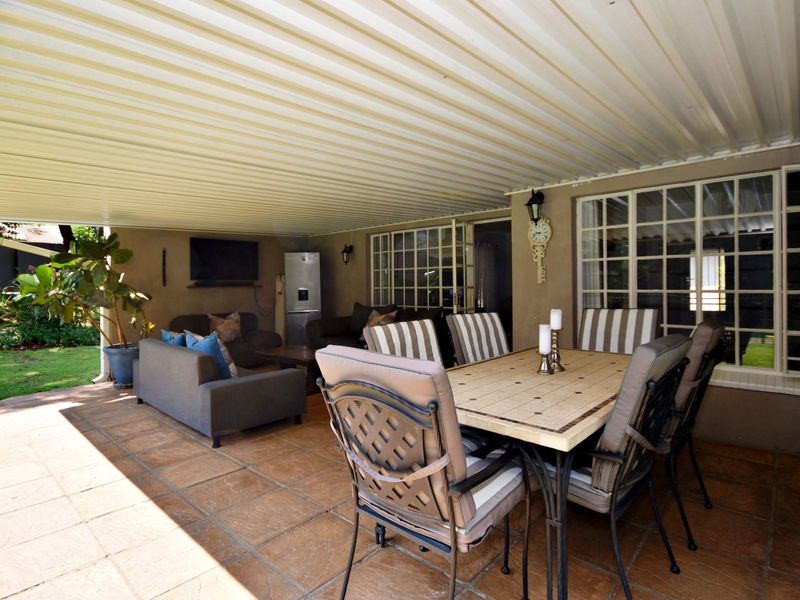 A spacious covered patio featuring tiled flooring and a corrugated metal roof, providing an ideal outdoor entertainment area overlooking the garden.