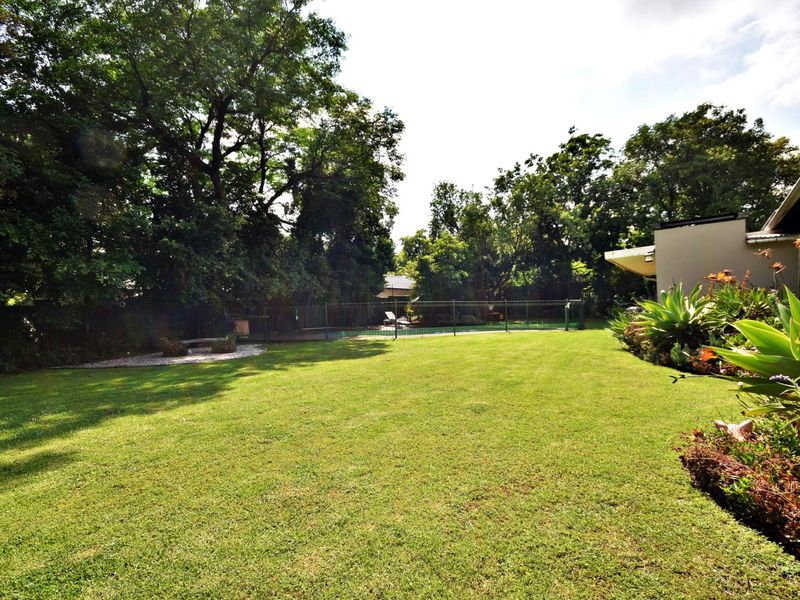 A spacious, well-maintained garden featuring a lush lawn, mature trees, and a fenced swimming pool area.
