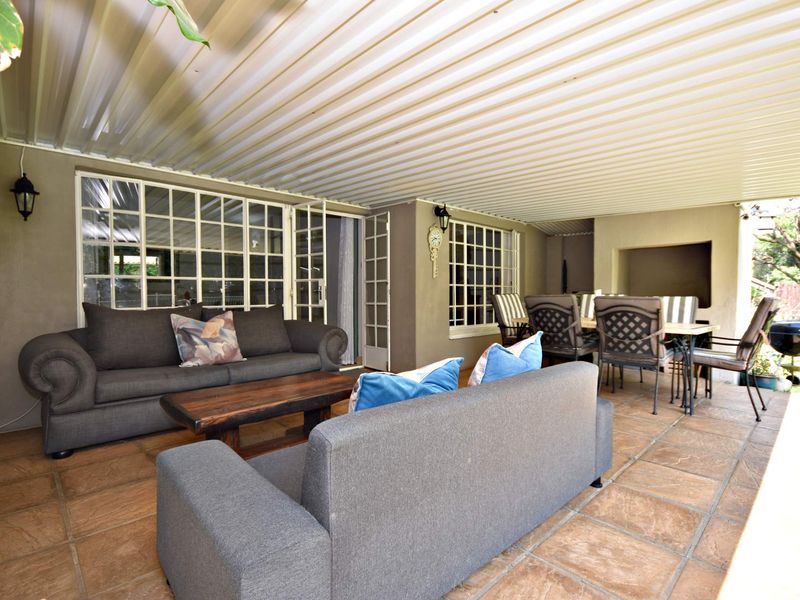 A spacious covered patio featuring tiled flooring, a built-in braai, and direct access to the home through classic french doors.
