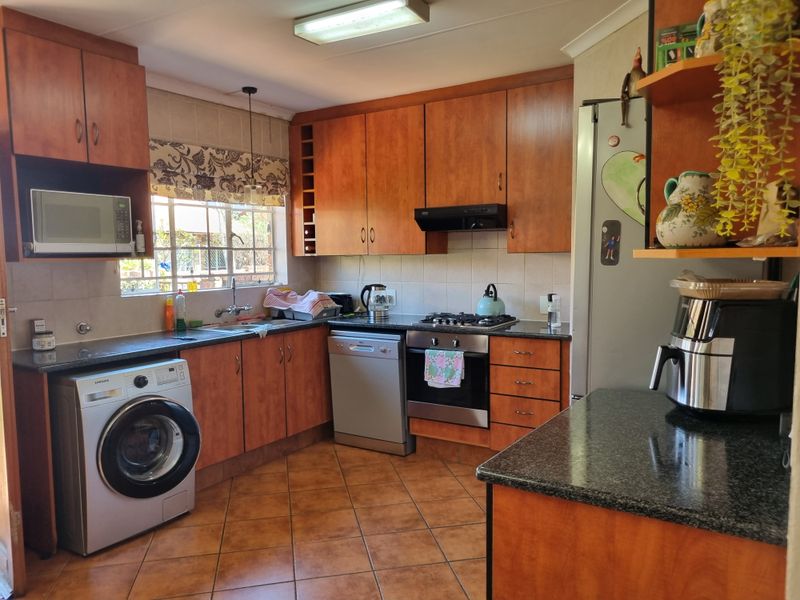 Functional kitchen featuring warm-toned wooden cabinetry, granite countertops, integrated gas hob, oven, and dedicated space for laundry appliances.