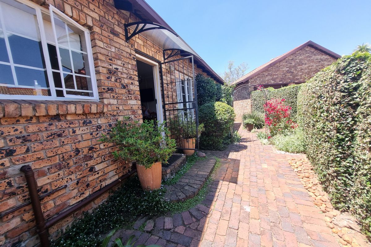 A well-maintained rear exterior view of the townhouse featuring a face brick facade, paved walkway, and established garden hedging.