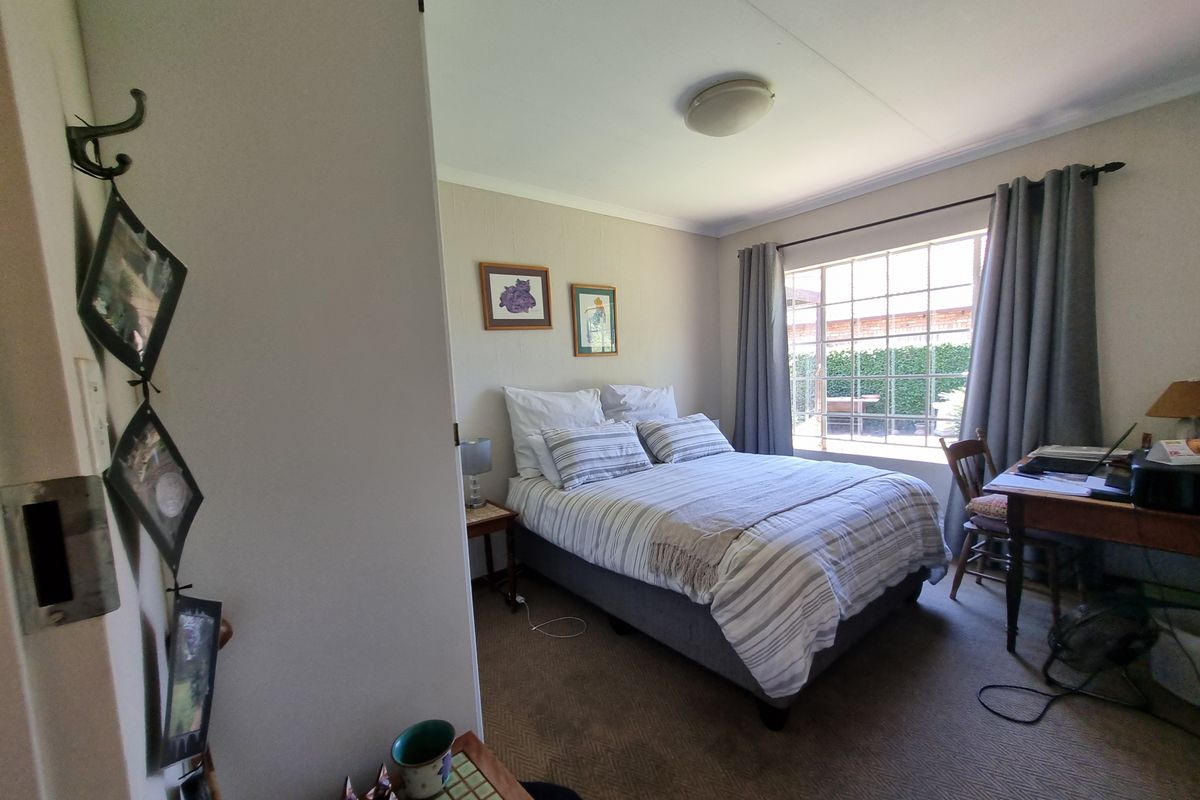 A cozy bedroom featuring carpeted flooring, a grid-pattern window providing natural light, and a neutral color palette.