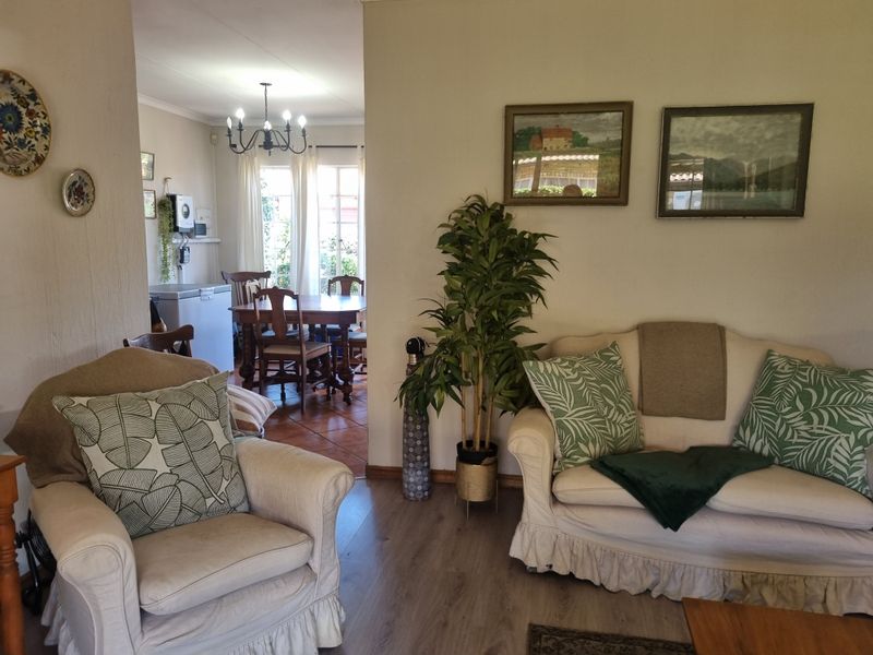 Open plan living and dining area featuring laminate and tiled flooring, with a chandelier and access to the garden through french doors.