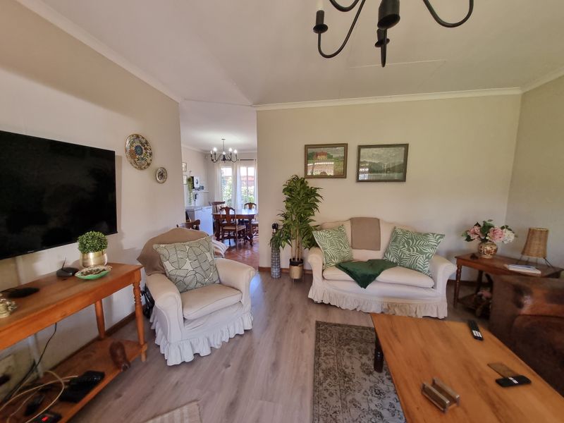 A comfortable living room featuring light-toned laminate flooring and a classic chandelier, with an open-plan flow leading into the adjacent dining area.