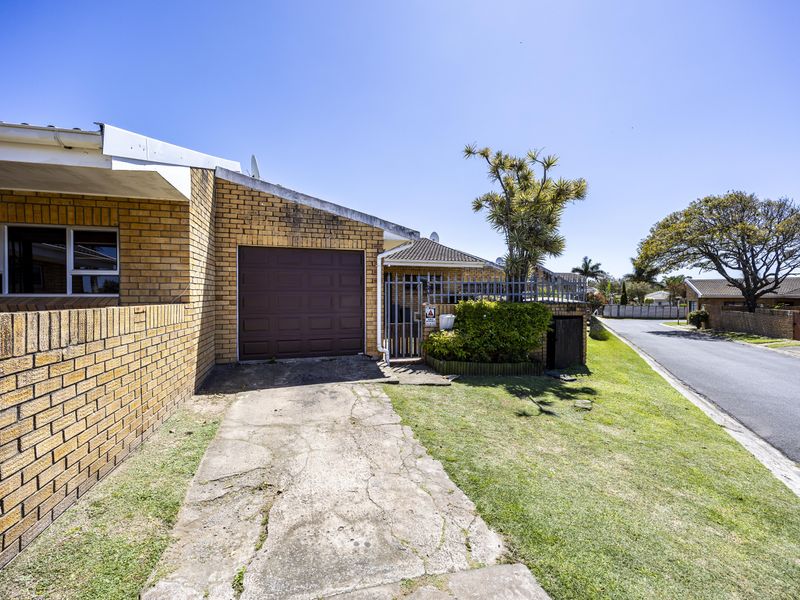 Front exterior view of a brick house featuring a single garage, concrete driveway, and perimeter security fencing in a residential street setting.