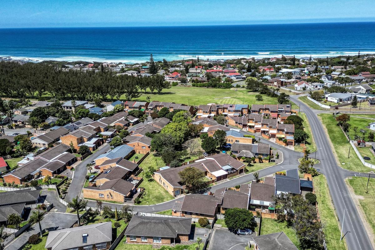An aerial view of a residential neighborhood situated near the coastline, showcasing the layout of houses, streets, and surrounding green spaces.