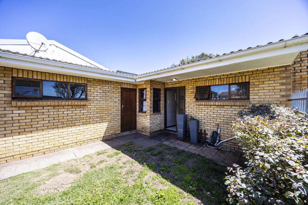 A rear exterior view of a face brick house featuring a paved courtyard area, security gate, and established garden space.