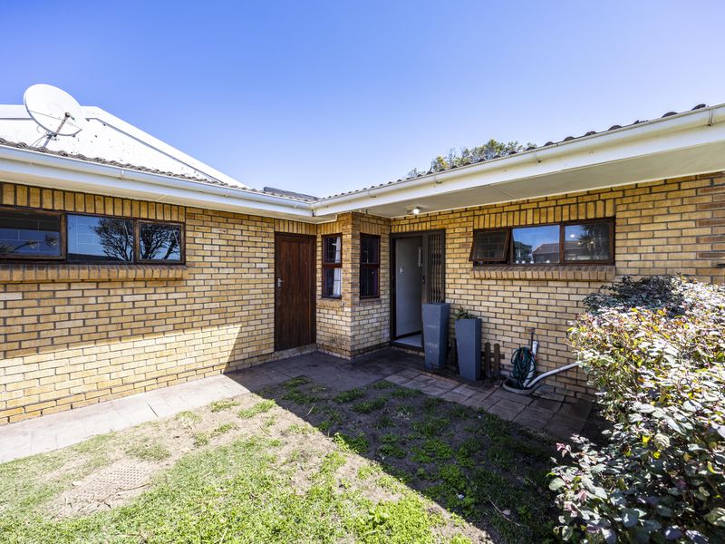 A rear exterior view of a face brick house featuring a paved courtyard area, security gate, and established garden space.