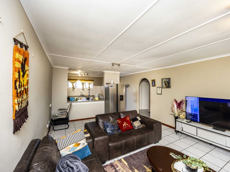 Open-plan living area featuring tiled flooring and an adjoining kitchen space with built-in cabinetry and sink.