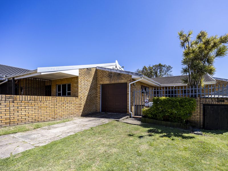 Front exterior view of a single-story brick house featuring a single garage, concrete driveway, and perimeter walling.