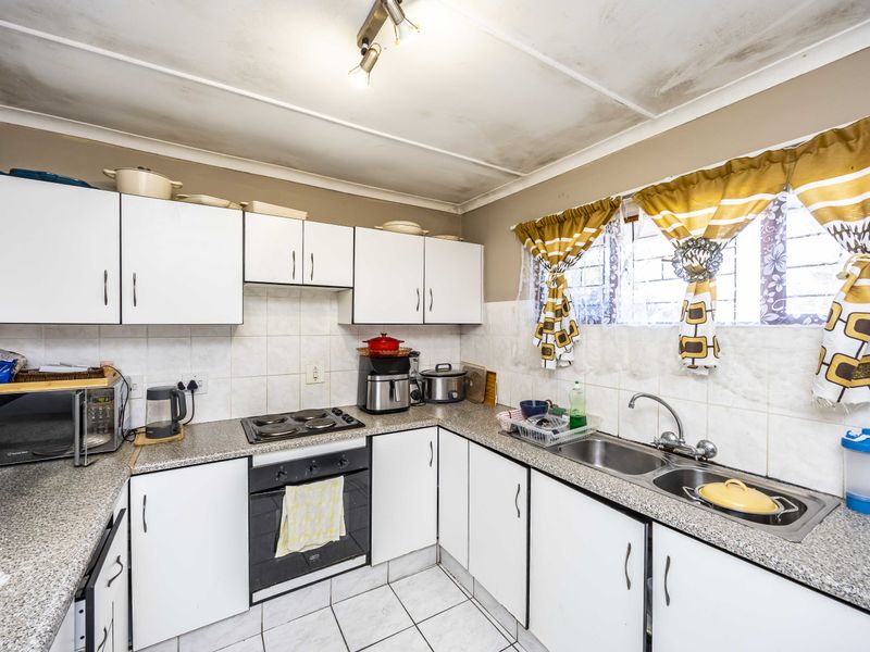 A functional kitchen featuring white cabinetry, laminate countertops, a double sink, and built-in oven with hob, requiring ceiling maintenance.