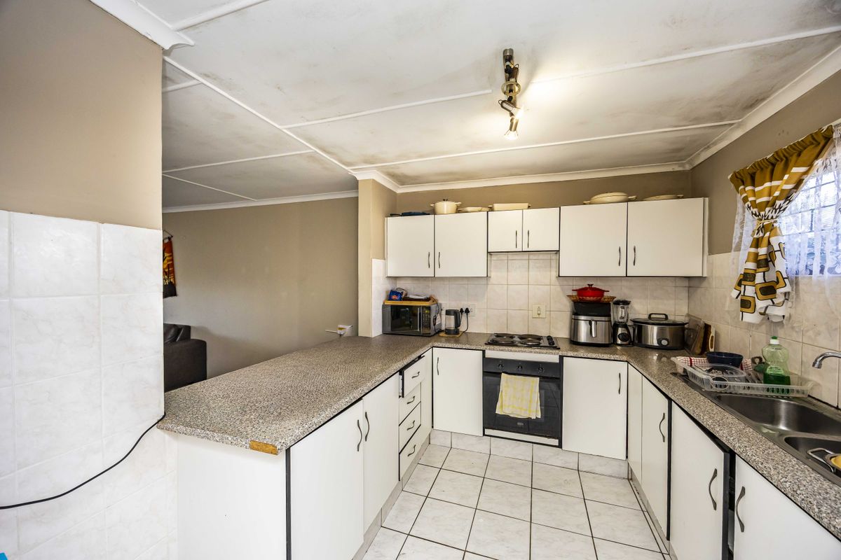 A functional kitchen featuring laminate countertops, built-in oven, hob, and tiled splashback, with white cabinetry and tiled flooring throughout.