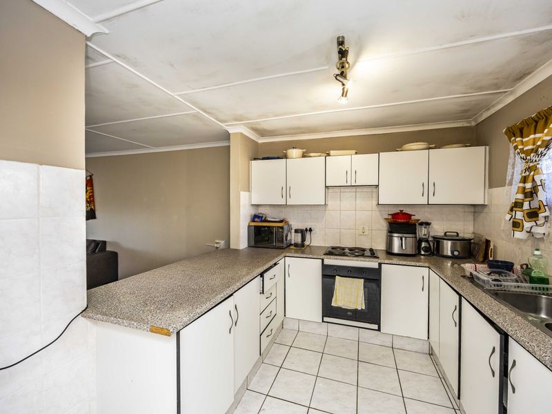 A functional kitchen featuring laminate countertops, built-in oven, hob, and tiled splashback, with white cabinetry and tiled flooring throughout.