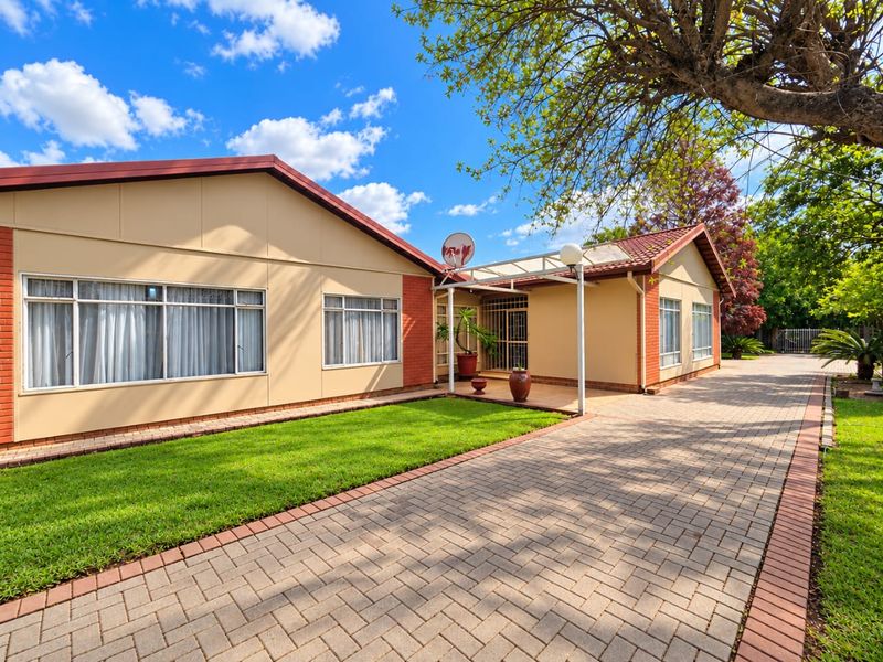 Well-maintained single-story residence featuring a paved driveway, brick and plaster facade, tiled roof, and a neat front lawn.