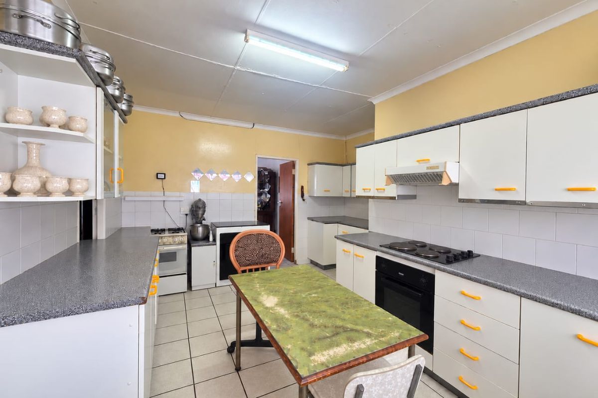 A functional kitchen featuring white cabinetry, laminate countertops, built-in oven, and electric hob, with tiled flooring and splashbacks throughout.