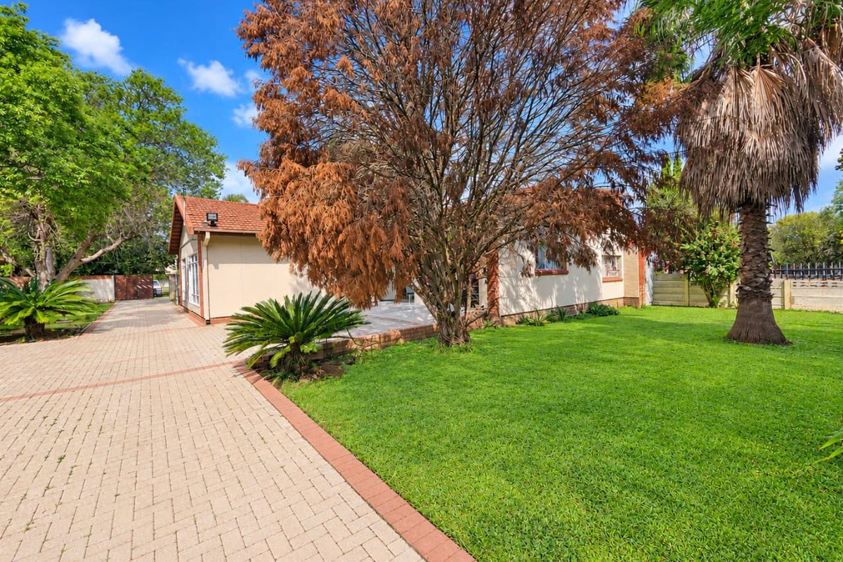 Rear view of the property featuring a paved driveway, well-maintained lawn, and established garden trees.