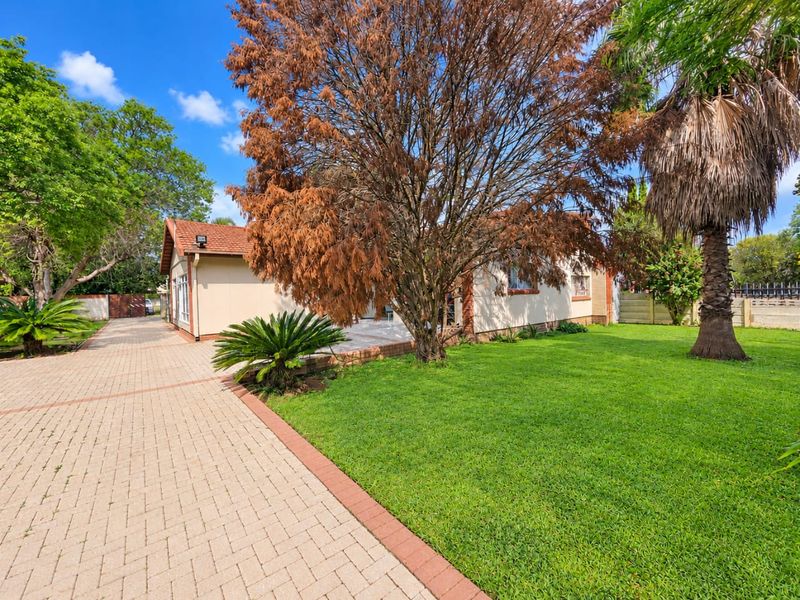 Rear view of the property featuring a paved driveway, well-maintained lawn, and established garden trees.