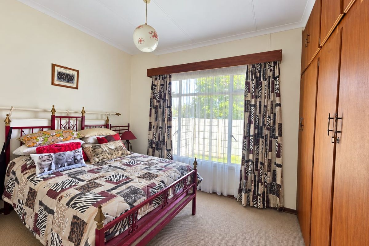 A well-maintained bedroom featuring built-in wooden cupboards, neutral carpeting, and a large window that provides natural light.