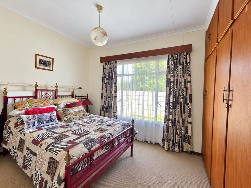 A well-maintained bedroom featuring built-in wooden cupboards, neutral carpeting, and a large window that provides natural light.