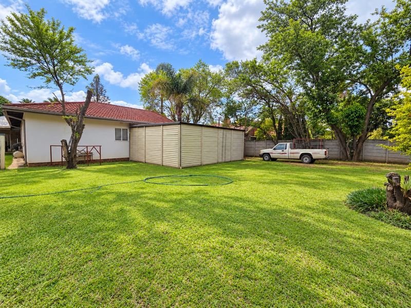Spacious rear garden featuring a well-maintained lawn, mature trees, a metal storage shed, and a secure precast concrete boundary wall.