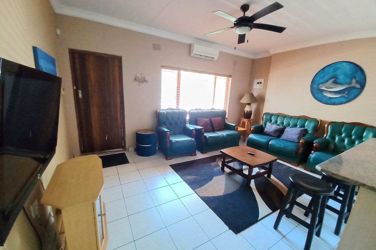 A functional living room featuring tiled flooring, a ceiling fan, and a wall-mounted air conditioning unit, providing a comfortable and climate-controlled living space.