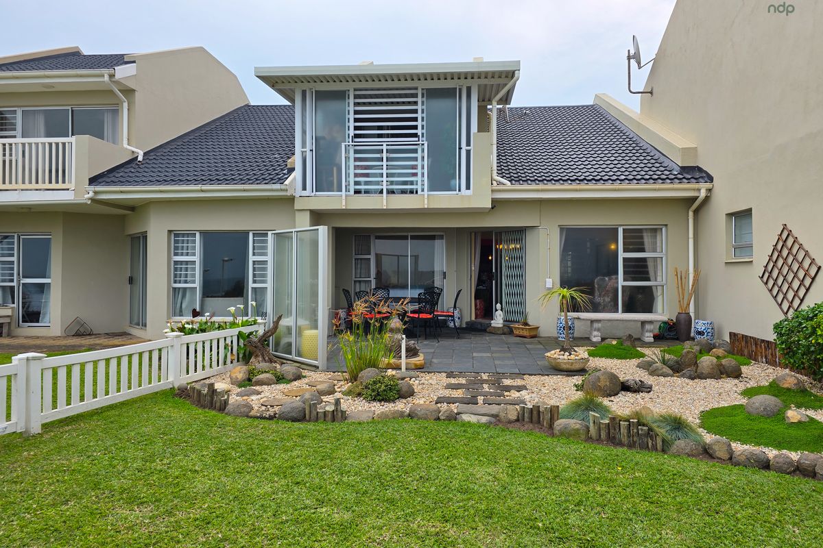 Rear view of the property featuring a landscaped garden, stone pathway, tiled patio area, and an upper-level balcony with sliding glass doors.