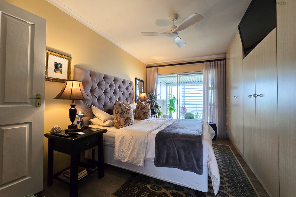 A well-maintained bedroom featuring built-in cupboards, a ceiling fan, and sliding glass doors that provide access to an outdoor patio area.