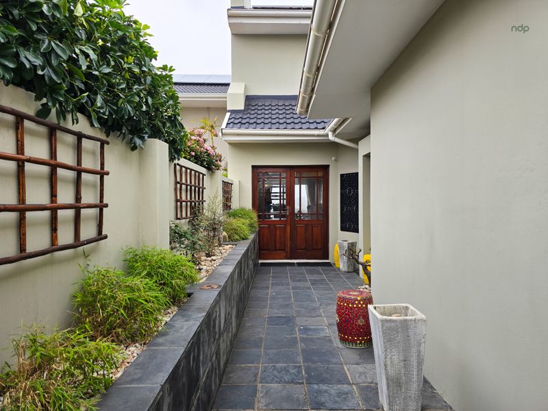 A well-maintained rear patio area featuring dark slate tiling, a raised stone planter with integrated bamboo, and classic wooden double door access.