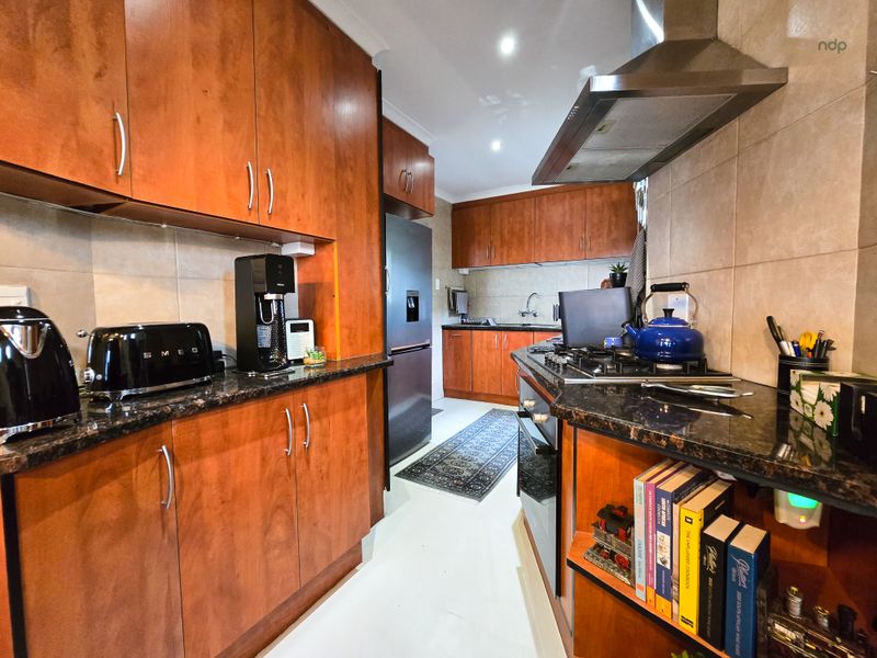 A functional kitchen featuring warm-toned wooden cabinetry, granite countertops, a gas hob with an extractor fan, and a tiled backsplash.
