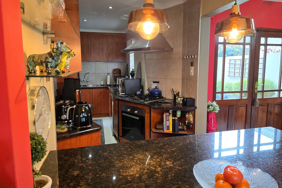 A functional kitchen featuring granite countertops, wooden cabinetry, built-in oven, gas hob, and a tiled backsplash, with direct access to the outdoor area.