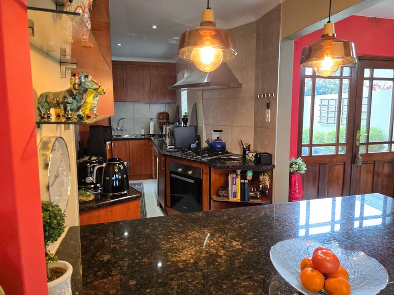 A functional kitchen featuring granite countertops, wooden cabinetry, built-in oven, gas hob, and a tiled backsplash, with direct access to the outdoor area.