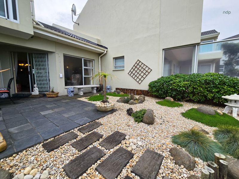 A well-maintained rear courtyard featuring a paved patio area, stone pathways, and landscaped garden beds with decorative rock features.