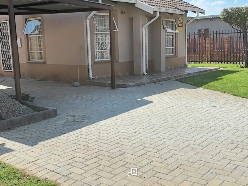Front exterior view of the house featuring a paved driveway, carport, and a small tiled entrance porch with security features.