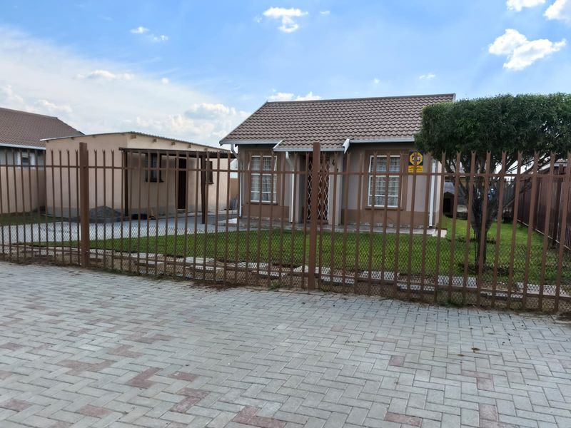 A well-maintained single-story house featuring a tiled roof, secure perimeter fencing, and a neat front lawn with a paved driveway.