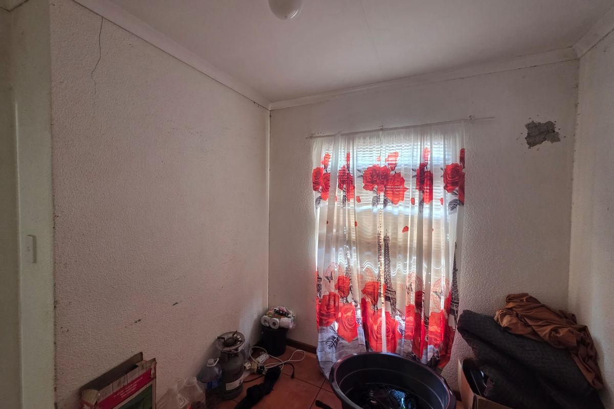 A bedroom featuring tiled flooring and a ceiling light fixture, currently requiring maintenance due to visible wall cracks and plaster damage.
