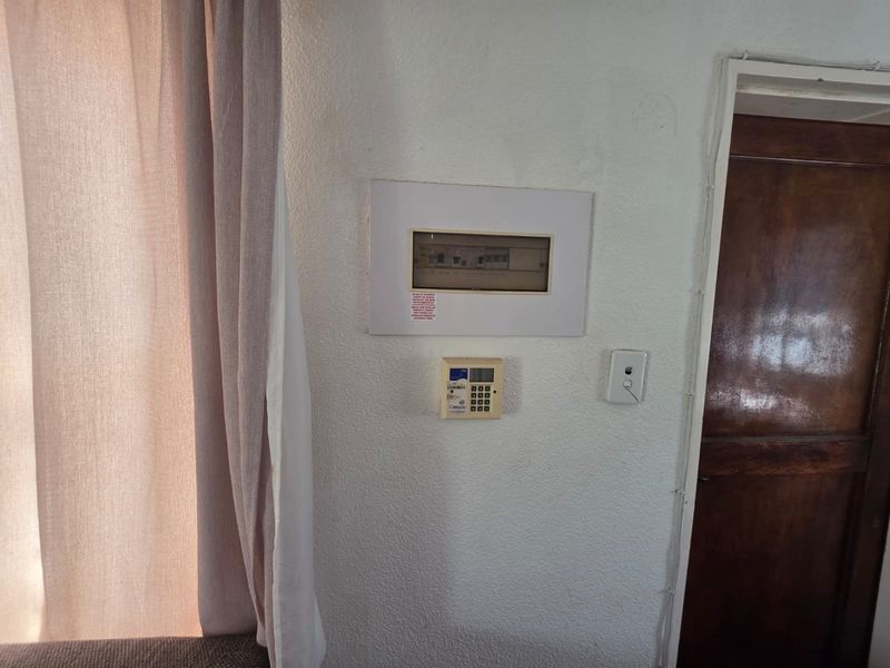 A utility wall area featuring a built-in electrical distribution board and an alarm system keypad next to a wooden door.