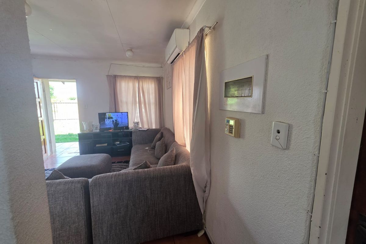 A living room featuring tiled flooring, a wall-mounted air conditioning unit, and a security alarm system, with direct access to an outdoor patio area.
