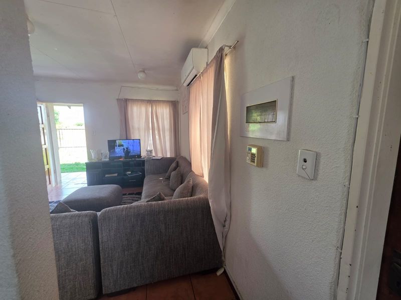 A living room featuring tiled flooring, a wall-mounted air conditioning unit, and a security alarm system, with direct access to an outdoor patio area.