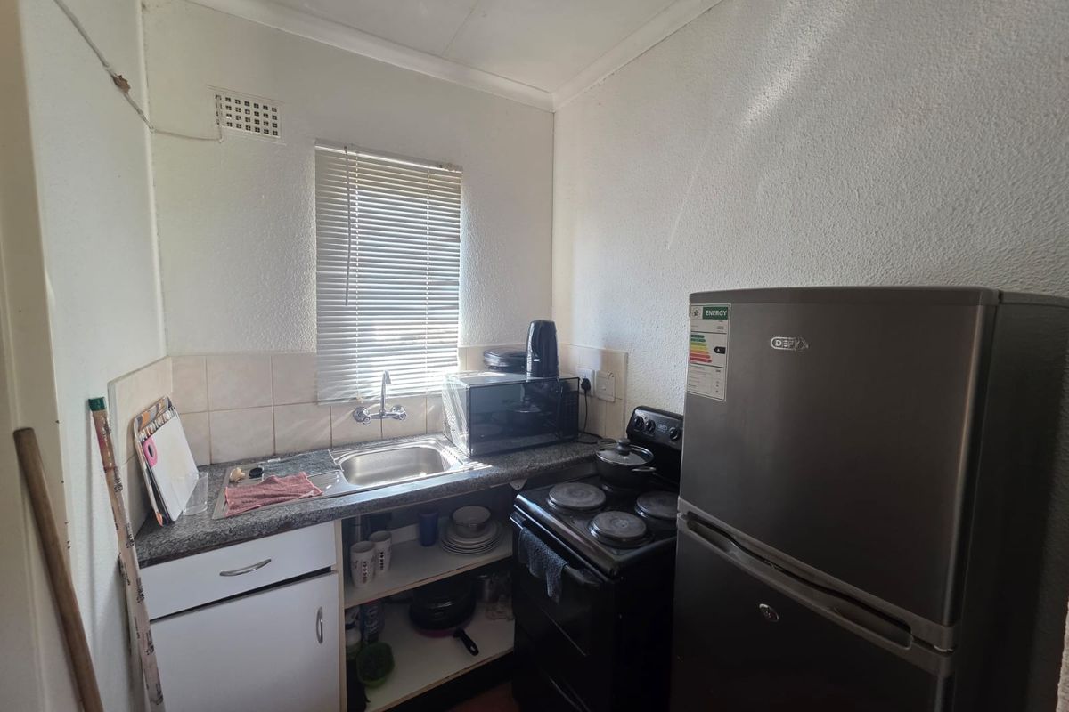 Compact kitchen featuring a stainless steel sink, laminate countertops, tiled splashback, and basic cabinetry, providing a functional space for meal preparation.