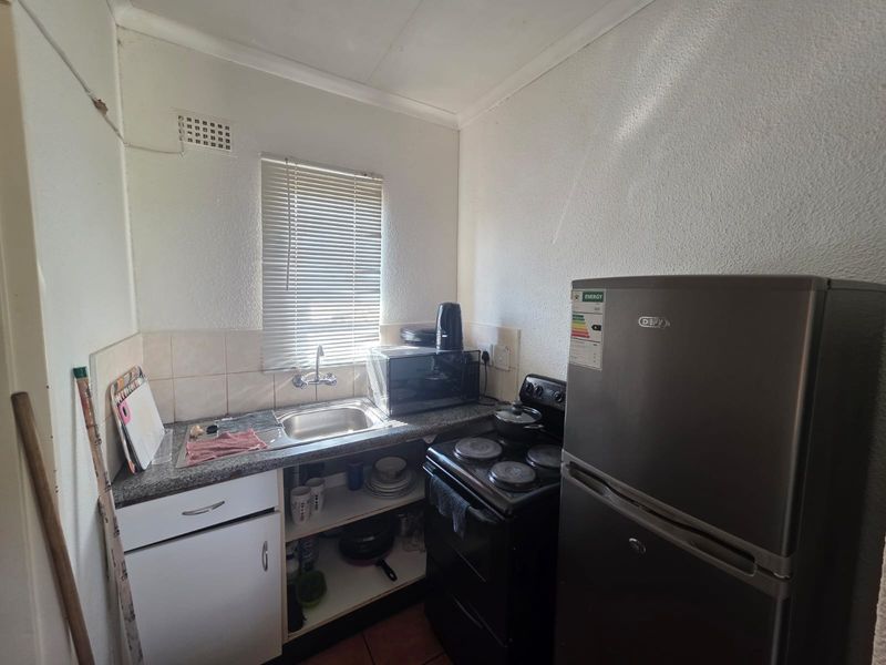 Compact kitchen featuring a stainless steel sink, laminate countertops, tiled splashback, and basic cabinetry, providing a functional space for meal preparation.