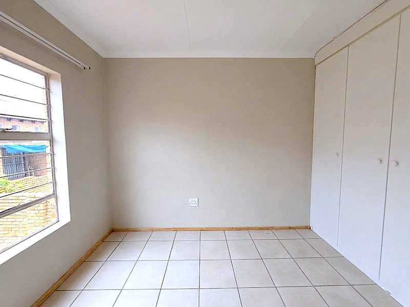 A vacant bedroom featuring neutral tiled flooring, built-in storage cupboards, and a steel-framed window providing natural light.