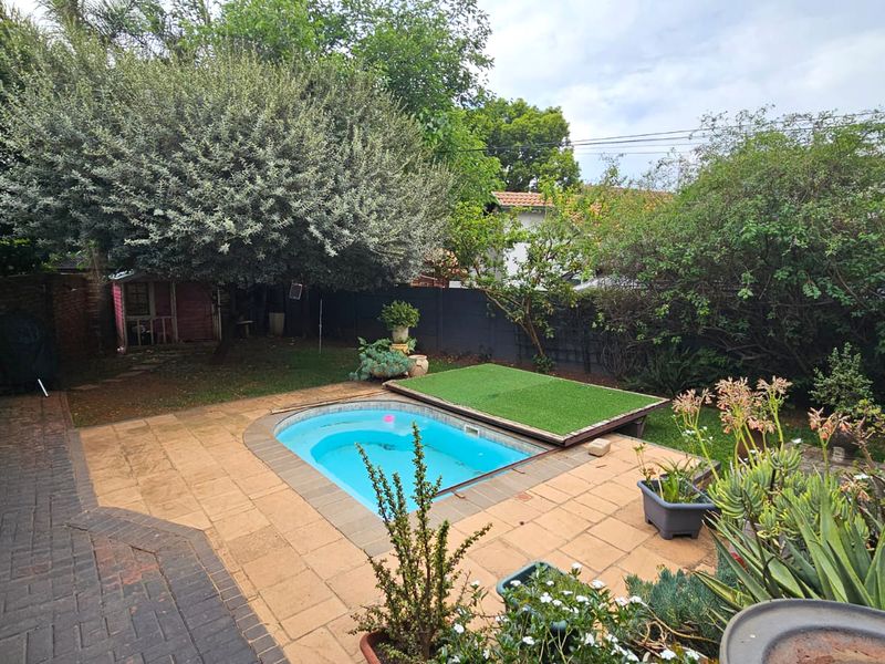 A backyard pool area featuring a paved patio, established garden landscaping, and a small swimming pool with a partial cover.