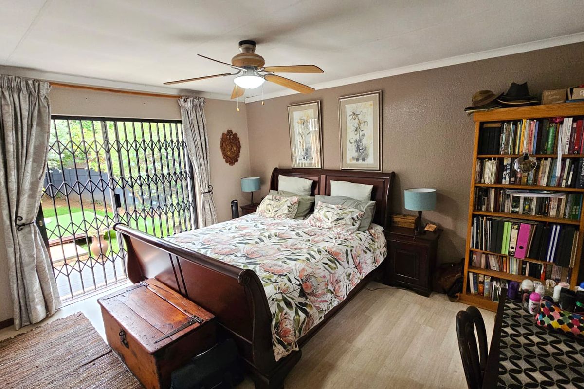 A well-maintained bedroom featuring laminate flooring, a ceiling fan, and a sliding glass door with a security gate providing access to the outdoors.