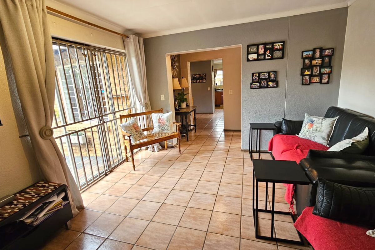 A living room featuring tiled flooring, a sliding glass door with a security gate, and access to an adjoining room.