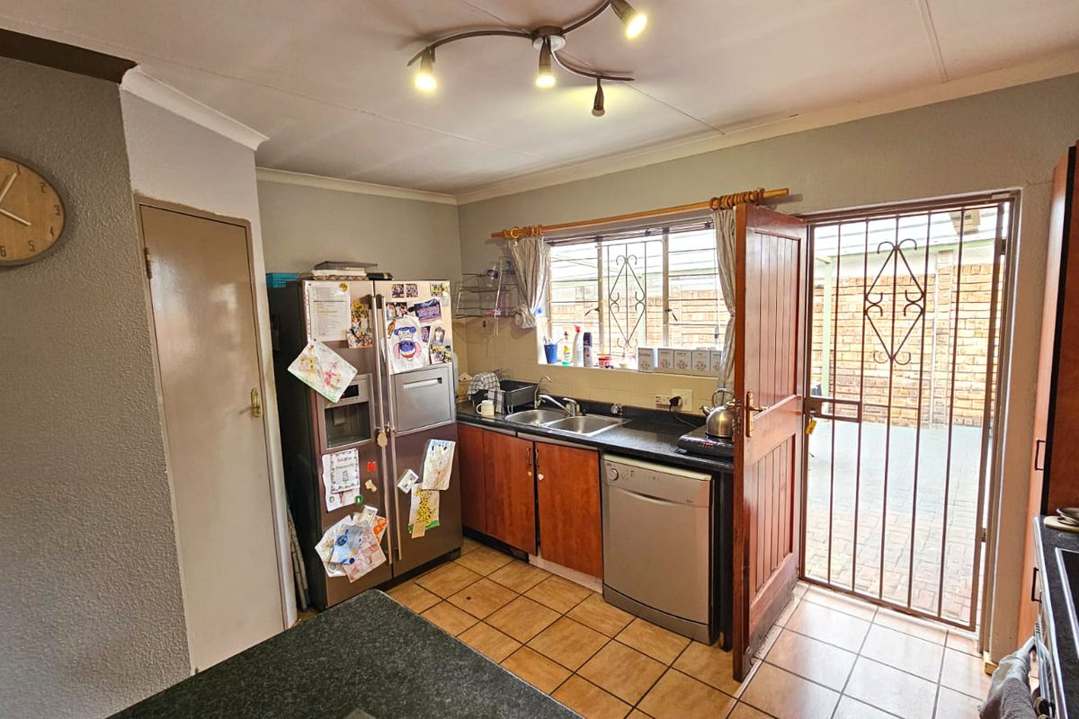 A functional kitchen featuring built-in cabinetry, a double sink, tiled flooring, and direct access to an outdoor area through a security gate.