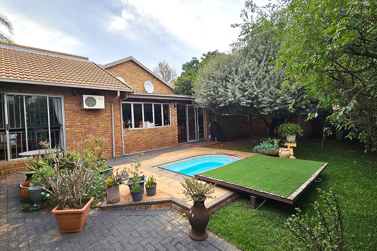 Rear exterior view of a brick duet property featuring a paved patio area, a small swimming pool, and established garden landscaping.